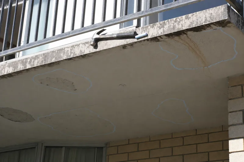 A hammer and a stick of chalk resting on a balcony edge, with chalk outlines drawn around hollow-sounding patches on the soffit below — illustrative example